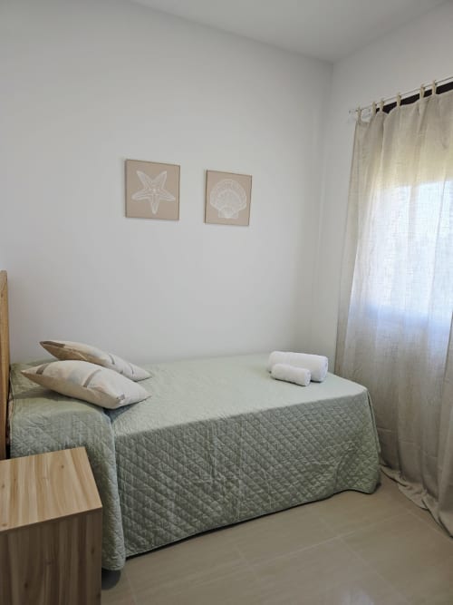 Dormitorio luminoso en apartamento frente al mar Ona vacaciones en Gandía con colcha acolchada verde, almohadas y decoración de tema marino