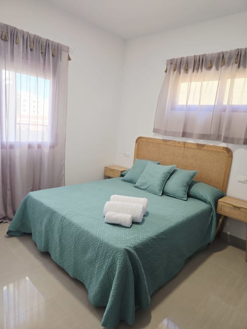 Dormitorio luminoso con ropa de cama turquesa, cabecero de ratán y toallas blancas en el apartamento Ona vacaciones en playa de Gandía