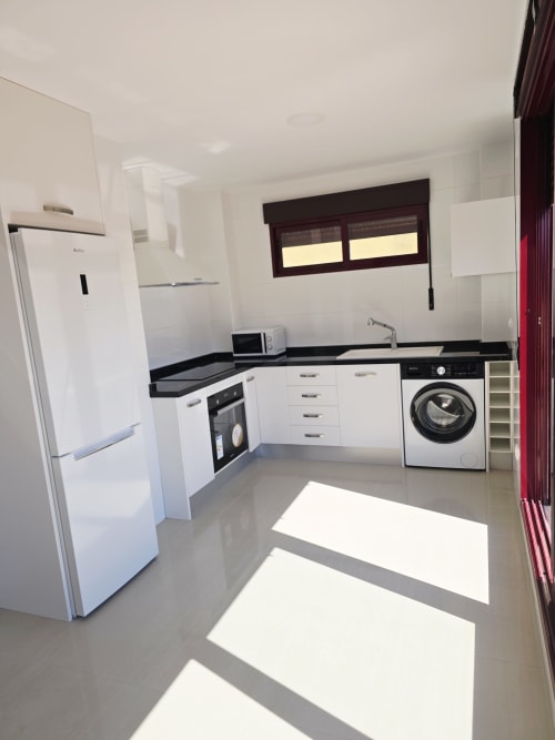 Cocina moderna en apartamento frente al mar en Ona vacaciones, Gandía con muebles blancos, encimeras negras y lavadora