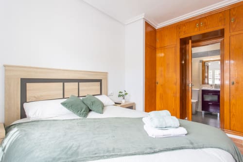 Moderno dormitorio en Villa ALROGA con cabecero de madera, ropa de cama verde y acceso a baño privado en San Pedro del Pinatar