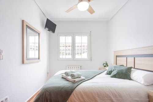 Moderno dormitorio con camas gemelas, almohadas verdes, ventilador de techo, TV montado en pared y ventanas con vista a San Pedro del Pinatar