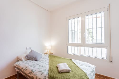 Dormitorio luminoso con camas gemelas, manta verde, lámpara de mesa y amplios ventanales con vistas a la piscina en villa Haus Holiday Homes