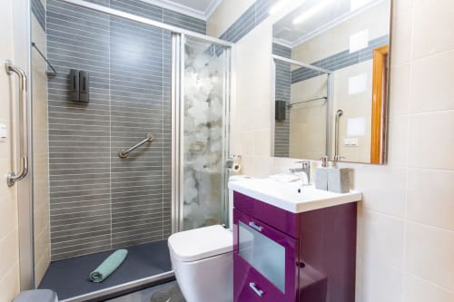 Baño moderno con ducha de azulejos grises, tocador púrpura y lavabo blanco en villa de San Pedro del Pinatar