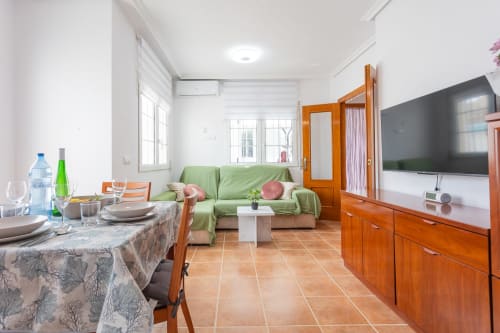 Sala de estar y comedor de planta abierta en Villa ALROGA, San Pedro del Pinatar, con sofá verde, muebles de madera y televisor plano