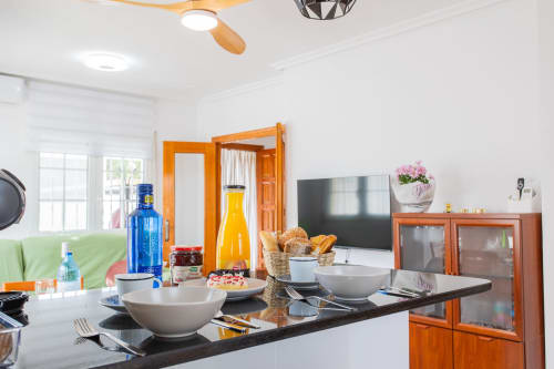 Cocina moderna de villa con encimera negra, boles blancos, botellas, cesta de pan y TV en San Pedro del Pinatar