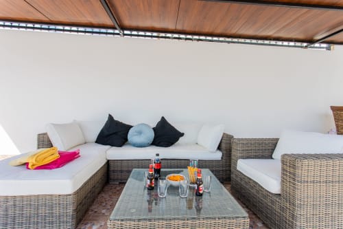 Zona de descanso al aire libre en Villa ALROGA con muebles de mimbre, cojines blancos y bebidas sobre la mesa