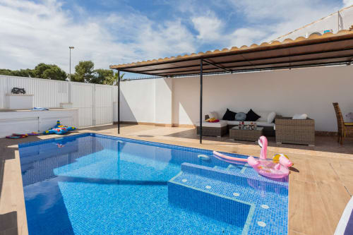Piscina privada con flotador de flamenco rosa, zona de descanso sombreada y villa blanca en Haus Holiday Homes, San Pedro del Pinatar
