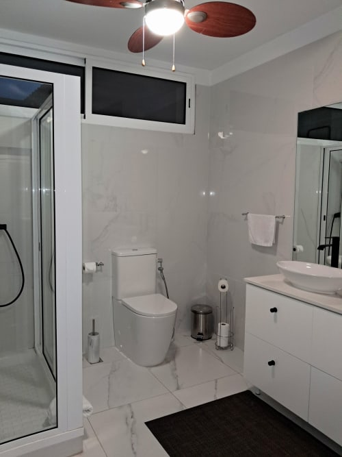Modern bathroom at Villa Supranee with white marble tiles, toilet, sink, walk-in shower, and ceiling fan