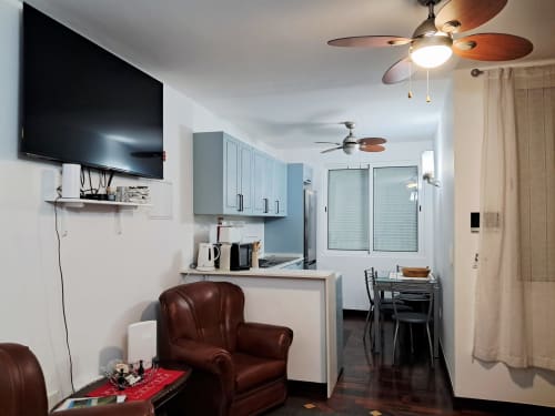 Modern apartment living area at Villa Supranee with brown leather chair, flat-screen TV, kitchenette, ceiling fans, and sea