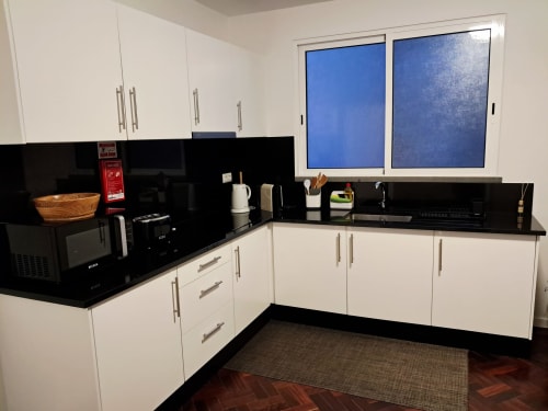 Modern white kitchen with black countertops and appliances in Villa Supranee apartment, Câmara da Lobos