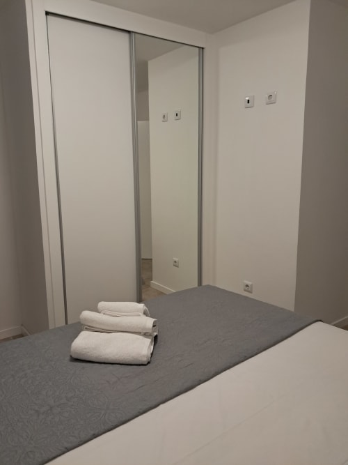 Modern bedroom at Villa Supranee in Câmara da Lobos with rolled towels on gray bed and mirrored wardrobe doors