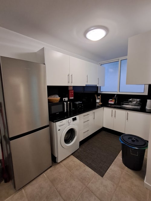Modern kitchen with white cabinets, black countertops, stainless steel appliances, and washing machine in Aldeia Supranee
