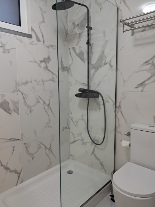 Modern bathroom shower enclosure with marble-pattern tile walls and black fixtures at Villa Supranee in Câmara da Lobos