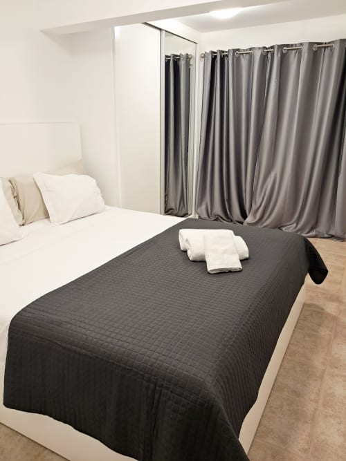 Modern bedroom at Villa Supranee in Câmara da Lobos with black quilted bed, white pillows, gray curtains, and city view