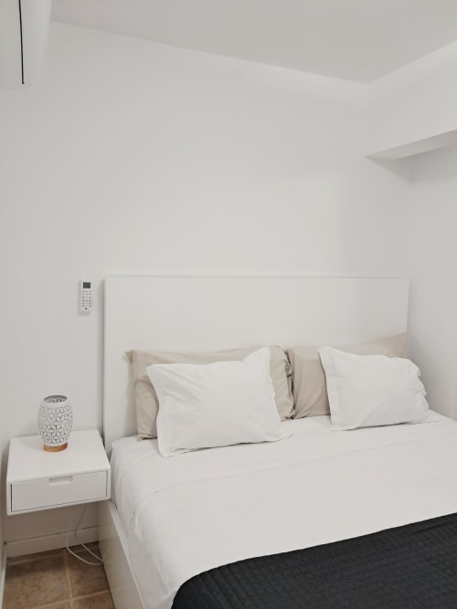 Modern minimalist bedroom at Villa Supranee with white bedding, neutral headboard, nightstand, and wall-mounted AC unit in