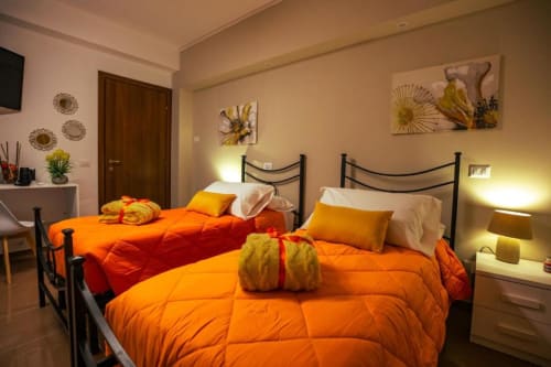 Camera Scirocco presso Torre dei Venti B&B con due letti, biancheria arancione, accenti gialli e illuminazione calda all'italiana
