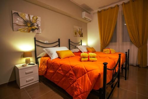 Camera Sirocco Torre dei Venti B&B con biancheria arancione, letto in ferro battuto nero, illuminazione calda e tende con vista sulla città