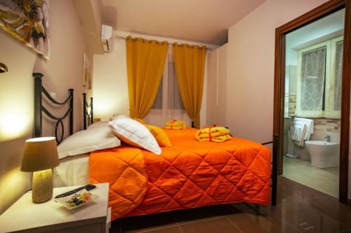 Camera Sirocco a Torre dei Venti B&B con trapunta arancione trapuntata, cuscini bianchi, tende dorate e bagno ensuite