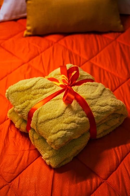 Asciugamani beige arrotolati con nastro rosso sulla biancheria da letto arancione della Camera Scirocco, Torre dei Venti B&B