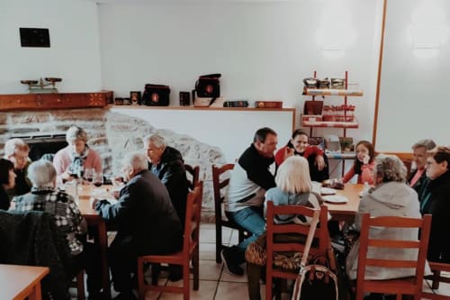 Grupo de comensales disfrutando de una comida en el restaurante Posada de Ollo en Ollo, España, con paredes de piedra rústica y sillas de madera roja