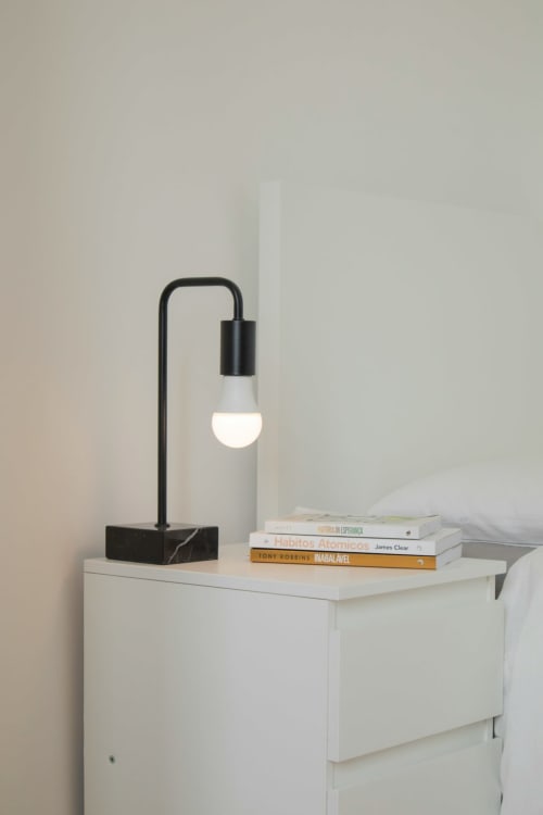 Moderna lampada da tavolo nera con base in marmo su comodino bianco a Borgo Luce, con libri impilati a Francavilla Marittima
