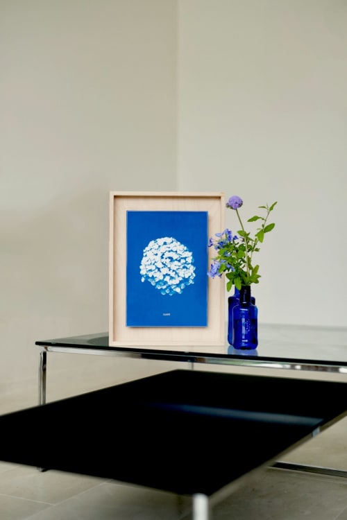 Arredamento moderno a Borgo Luce: quadro blu incorniciato con fiori bianchi, vaso in vetro blu con fiori viola, tavolo minimalista