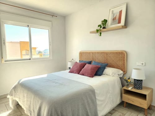 Dormitorio moderno en BAKIT HOUSE en Águilas con cabecero de ratán, almohadas coloridas, mesita de noche de madera y vistas a la ciudad