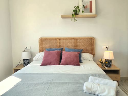 Dormitorio moderno con cabecero de ratán, cojines coloridos y mesillas de madera con lámparas en BAKIT HOUSE, Águilas