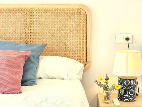 Dormitorio moderno con cabecero de ratán, cojines coloridos y lámpara de noche con flores amarillas en el apartamento BAKIT HOUSE de Águilas