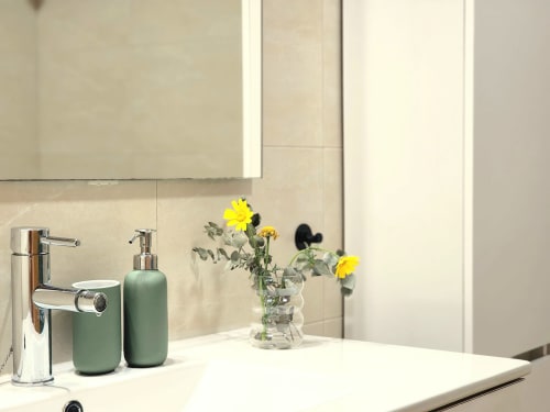 Vanidad de baño moderno en BAKIT HOUSE Águilas con grifo cromado, dispensadores de jabón verde y flores amarillas en jarrón de cristal