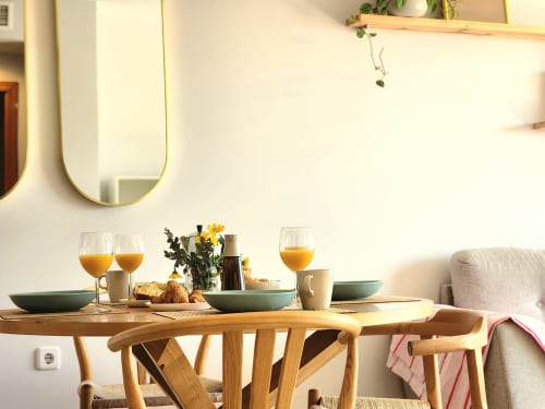 Comedor luminoso en BAKIT HOUSE en Águilas con mesa de madera, zumo de naranja fresco y vistas a la ciudad a través de amplias ventanas.