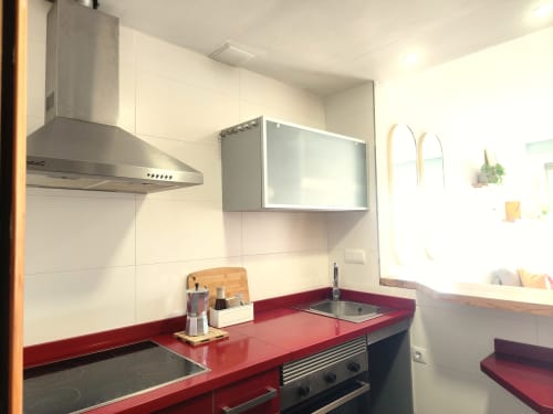 Cocina moderna con encimera roja, electrodomésticos de acero inoxidable y muebles blancos en apartamento BAKIT HOUSE en Águilas