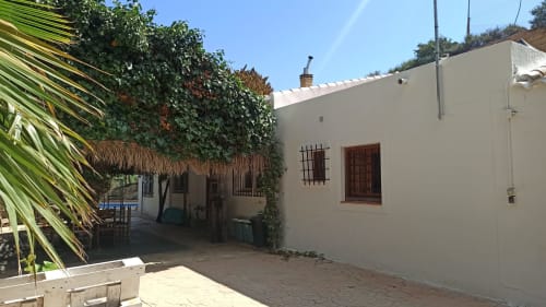 Villa Bakit en Águilas con fachada de muros blancos, puertas de terracota, paredes cubiertas de hiedra y palmeras en su patio