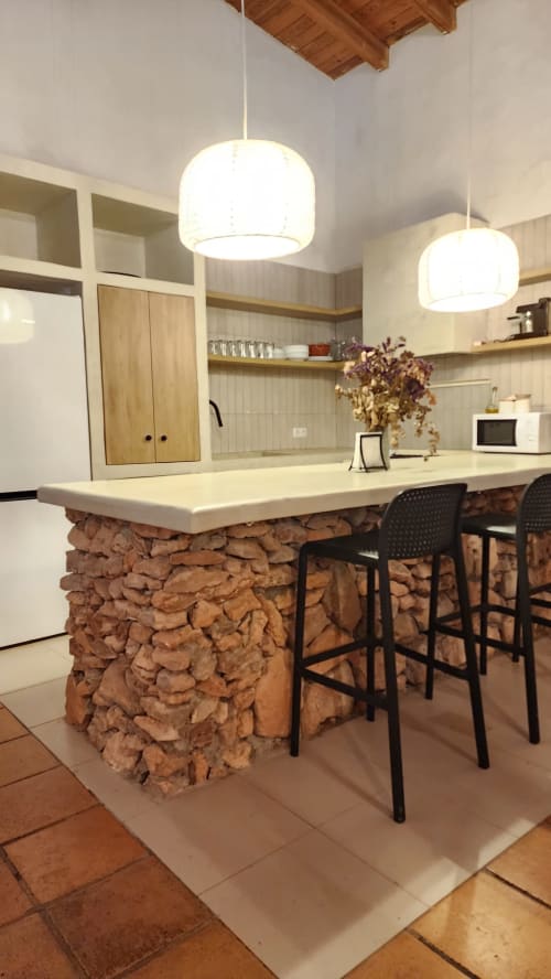 Cocina moderna con isla de piedra, lámparas colgantes blancas y muebles de madera en la villa Bakit House en Águilas