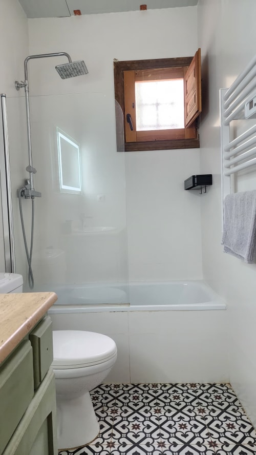 Baño moderno de la villa Bakit House en Águilas con ducha, inodoro, ventana de madera, toallero y azulejos decorativos