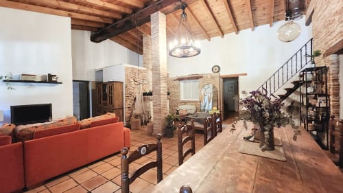 Amplia sala de estar de la villa Bakit House en Águilas con ladrillo visto, vigas de madera, sofá rojo y escalera
