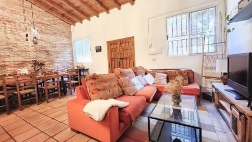Luminosa sala de estar de la villa Bakit House en Águilas con sofá naranja, vigas de madera vista y amplios ventanales