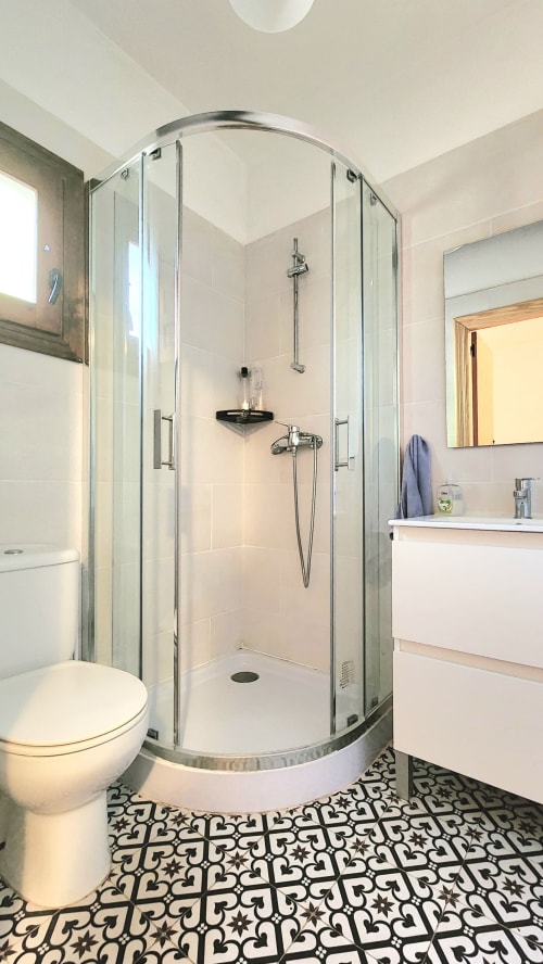 Baño moderno en villa Bakit House en Águilas con ducha de cristal curvo, sanitarios blancos y piso con azulejos estampados