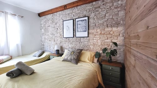Dormitorio de la villa Bakit House en Águilas con pared de ladrillo, vigas de madera, ropa de cama crema y cuadros enmarcados