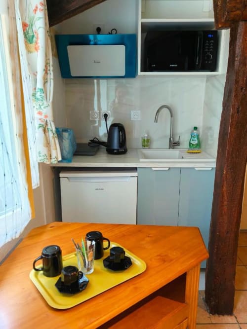 Kitchenette Le Coin des Artistes avec table orange, électroménagers noirs et armoires bleues dans la chambre Pastel