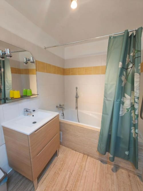Salle de bain moderne au Coin des Artistes avec vanité en bois, baignoire, rideau de douche vert et murs carrelés