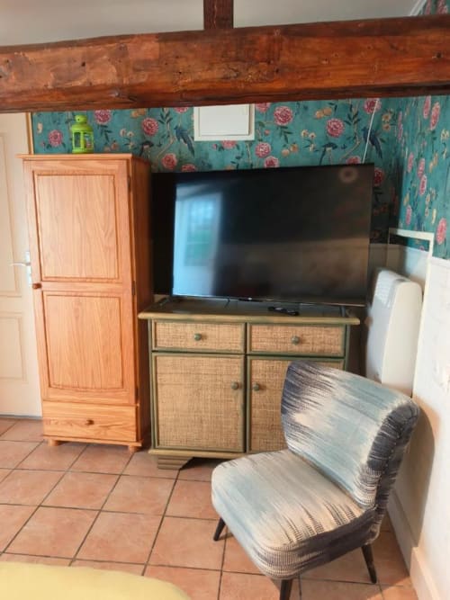 Chambre pastel au Coin des Artistes avec télévision, penderie en bois, fauteuil texturé et papier peint floral