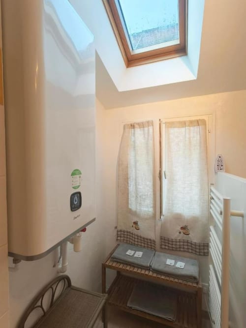 Salle de bains lumineuse à Le Coin des Artistes BnB avec puits de lumière, murs blancs, rideaux crème et chaudière blanche moderne