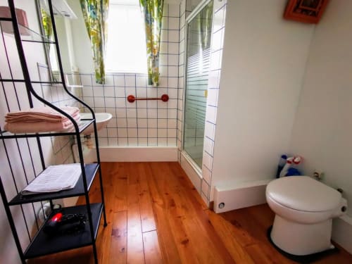 Salle de bain moderne au Coin des Artistes avec sol en bois, douche, toilettes, porte-serviettes et plantes vertes
