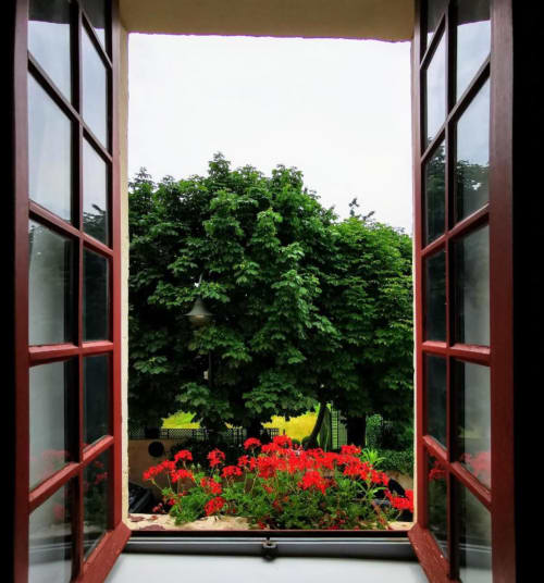 Portes-fenêtres aux cadres rouges ouvertes sur le jardin Le Coin des Artistes avec fleurs rouges éclatantes et arbres verdoyants