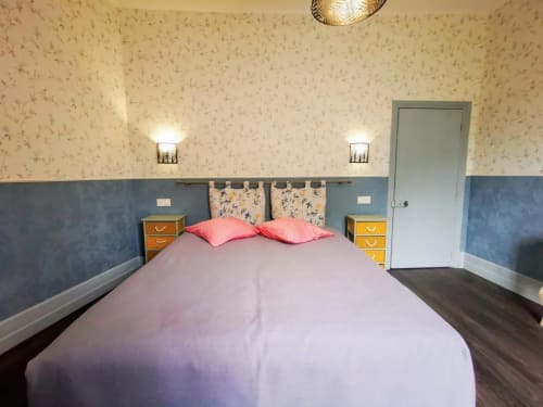 Chambre à Le Coin des Artistes avec lit double, oreillers roses, deux tables de nuit et papier peint bleu crème