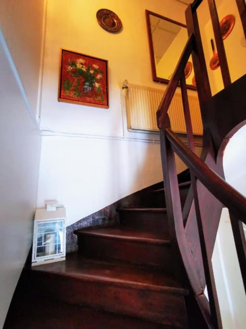 Escalier en bois avec rampe noire à Le Coin des Artistes B&B, murs décorés d'œuvres d'art encadrées