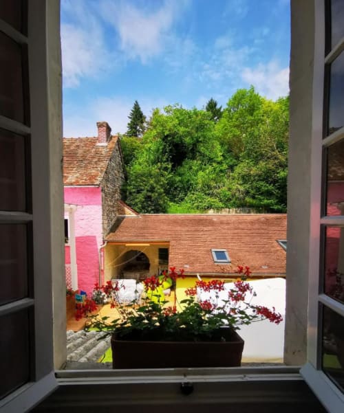 Vue depuis la fenêtre de la chambre Le Coin des Artistes sur une cour colorée avec fleurs rouges et bâtiments en brique