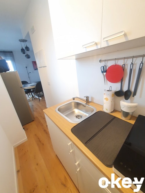 Moderna cucina in appartamento fronte mare a Bari con lavello, piano cottura, tagliere rosso e utensili sospesi su ripiano in legno