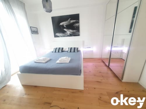 Camera da letto moderna in appartamento fronte mare a Bari con letto blu, cuscini rigati, opera con delfini, armadio specchiato e legno